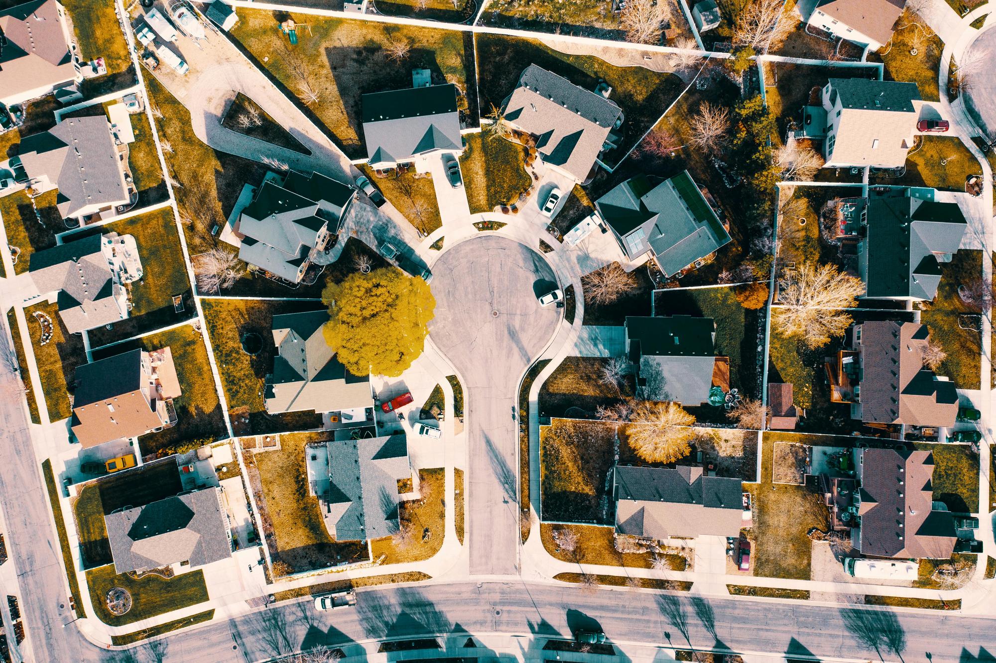 Aerial view of a cul-de-sac neighborhood with detached homes on separate fenced lots, tree-lined yards, and a loop of paved street running between the parcels.