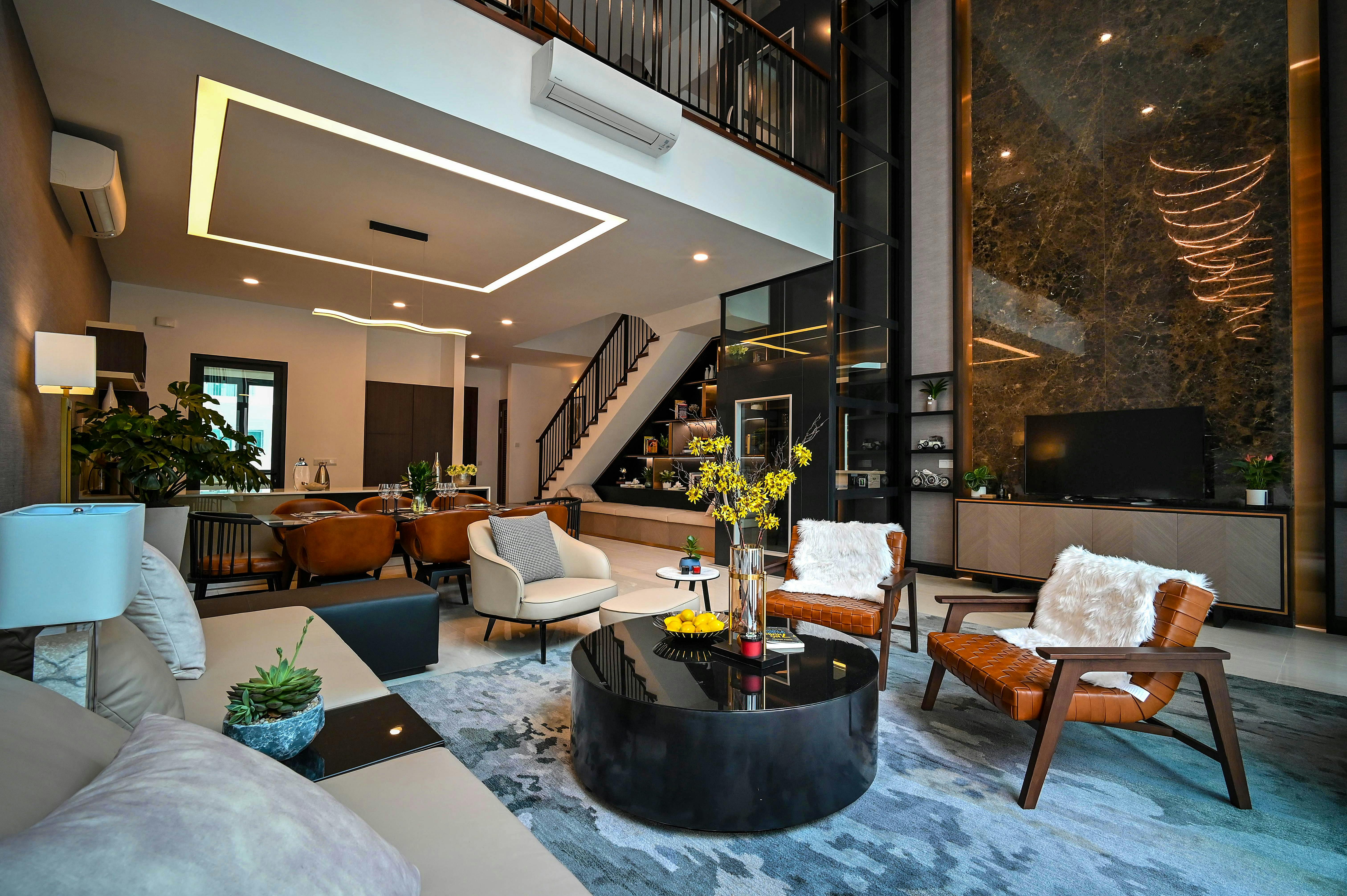 A modern open-concept living and dining room with dark marble feature wall, leather armchairs, and a mezzanine loft with black railings.