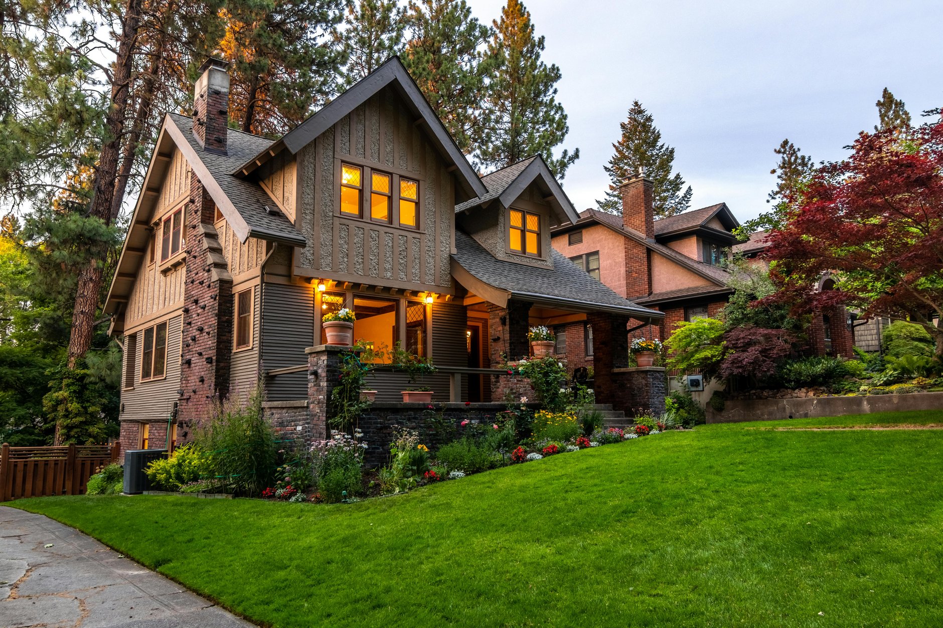A two-story Craftsman-style house with a stone porch and sloping front lawn at dusk.