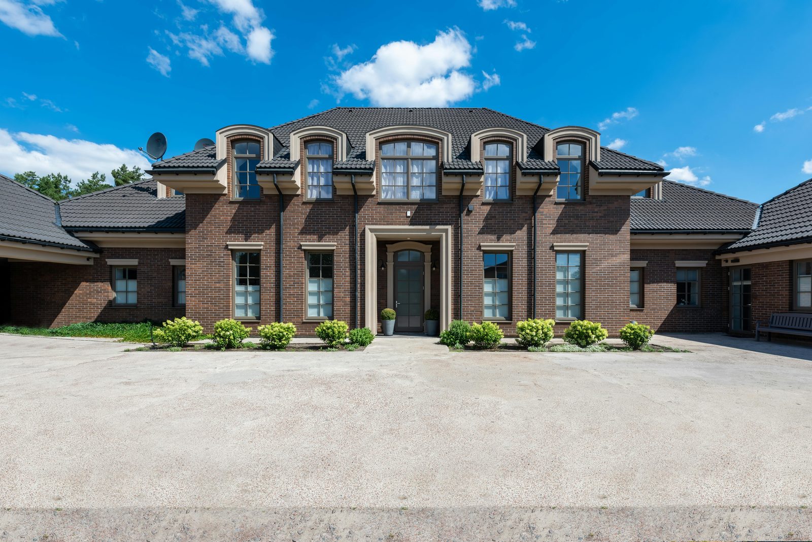 A brick house with a gabled roof and dormers on a green lot.